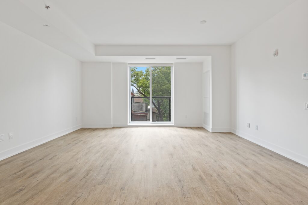 Logement vide, mur blanc et parquet bois clair avec une baie vitrée vue dégagée sur un arbre