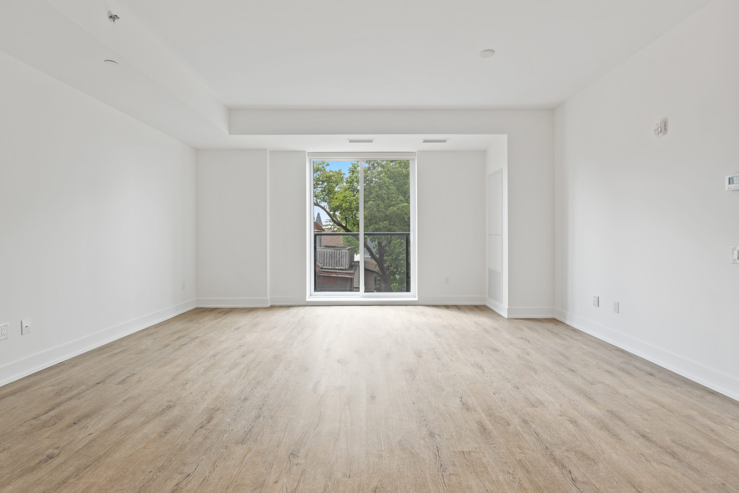 Logement neuf, mur blanc et parquet bois clair avec une baie vitrée vue dégagée sur un arbre